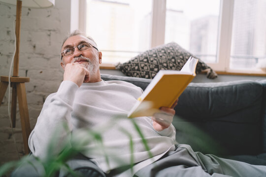 Impressed man thinking of book story while sitting on sofa