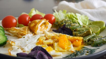 For breakfast, delicious scrambled eggs with vegetables and fresh tomatoes. With a fork, take a piece of scrambled eggs and green beans. Breakfast on a keto diet is rich in fats and proteins.