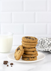 A bowl of freshly baked chocolate chip cookies and a glass of milk in a white kitchen. Copy space. National Cookie Day.