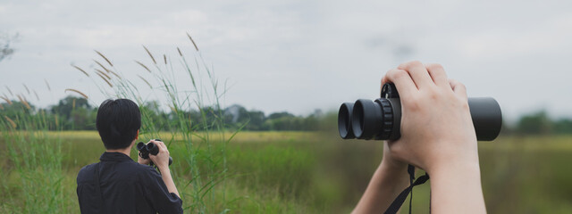A bird watcher is using a binoculars to search bird in the field. Concept of bird watching,...