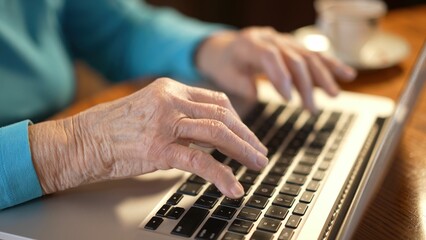 Obraz na płótnie Canvas Extreme closeup of elderly womans hands while she types on laptop computer keyboard.