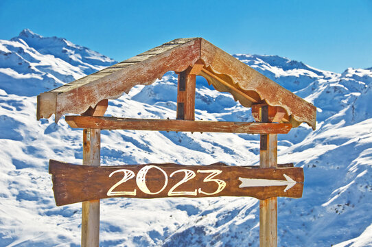 2023 written on a wooden direction sign, snowy mountain landscape on the background, ski new year card