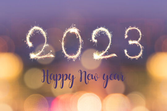 Happy new year 2023 written with sparkes on blurred bokeh lights background, holiday greeting card
