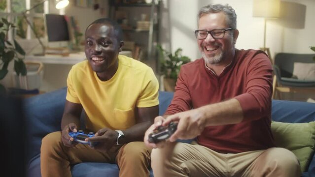 Multiethnic male friends sitting on sofa at home and playing console game together