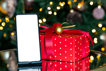 The concept of New Year and Christmas discounts and shopping. Digital phone with isolated screen on the background of the Christmas tree, bokeh and garland. new year gift box.