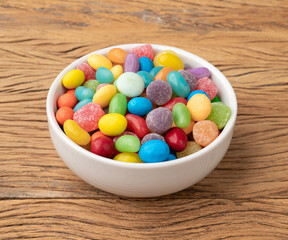 Assorted colorful candies in a bowl over wooden table