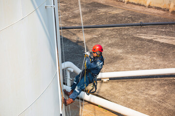 Male worker rope access industrial working at height tank oil wearing harness, helmet safety equipment rope access inspection of thickness tank