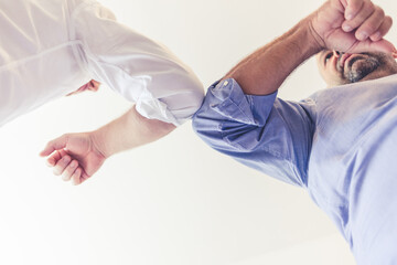 Shot of two businessmen bumping elbows in an office. Shot of a young businessman standing with a colleague in the office and giving him an elbow bump.