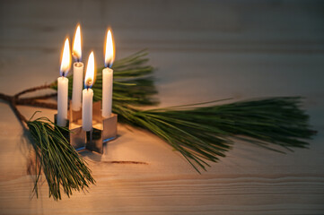 Four small advent candles placed on a cookie cutter in star shape and a pine branch on a wooden...