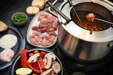 German fondue with raw meat and vegetables to be fried on long forks in a pot with boiling oil,...