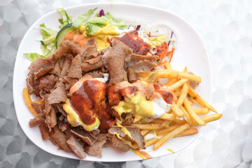 Doner kebab on a plate with French fries, salad and various sauces, popular fast food from Turkish...