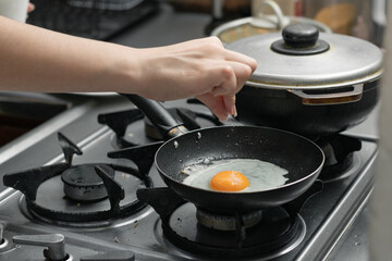 detailed shot of a woman's hand adding salt to the egg she is frying in a frying pan on the burner of a gas stove in a Colombian kitchen.