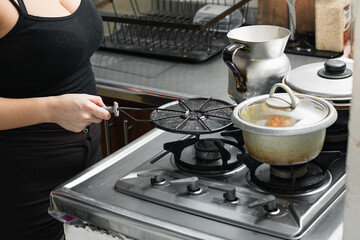 young woman in her kitchen holding a grill to grill arepas, placing it on top of a gas stove....