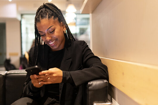 Cheerful black woman using smartphone in cafe