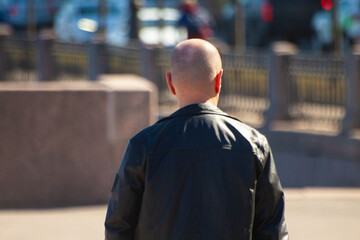 A man in a black jacket from the back walks forward in the spring through the city
