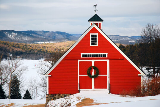 A small red barn, nestled in the highlands, is decorated with a wreath for Christmas and surrounded by snow in winter