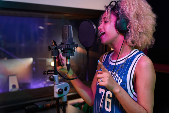 Cheerful female singer reading lyrics on smartphone while recording song