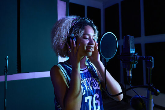 Female singer in headphones recording song in studio