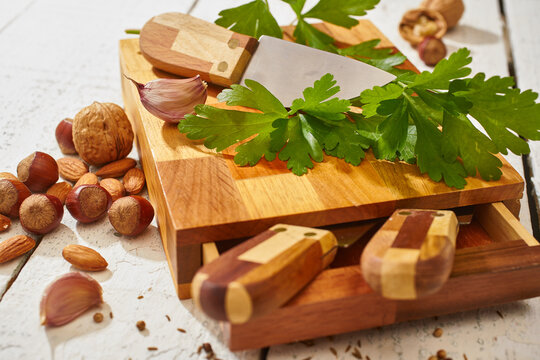 Assorted nuts and garlic with greens on cutting board with knife
