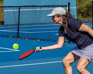 Young woman bends to dink the ball over the net during pickleball