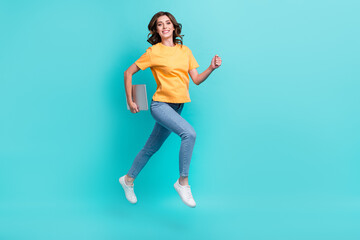 Fototapeta na wymiar Full length photo of shiny adorable lady wear yellow t-shirt jumping high holding modern gadget isolated turquoise color background