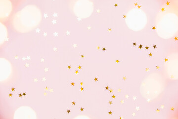 Defocused christmas festive background. Gold party decorations, confetti stars, christmas lights on pastel pink background. Christmas, winter holiday, new year concept. Flat lay, top view, copy space.