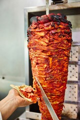 Vertical shot of a cook cutting meat off a spinning doner grill onto bread