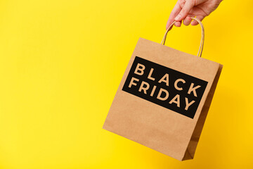 Black Friday, female hand holding brown craft shopping bag on yellow background. Black friday sale,...