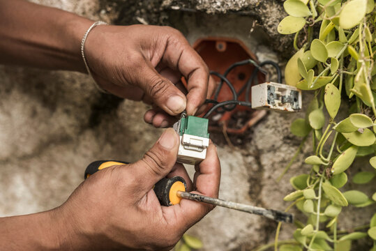 An electrician installs a new electrical outlet onto a junction box placed on an outdoor wall, hooking up the wires. 240 volt receptacle replacement.