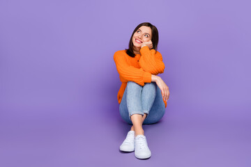 Fototapeta na wymiar Full body photo of stunning young girl sit look dreamy empty space dressed stylish orange knitted look isolated on purple color background