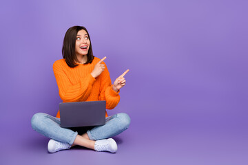 Full length photo of nice young woman netbook point empty space dressed stylish knitted orange outfit isolated on purple color background