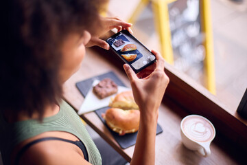 Woman In Coffee Shop Taking Picture Of Food To Post On Social Media
