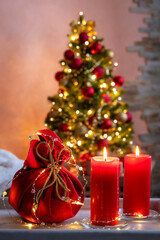 A bag with gifts and two red candles on a wooden table in the living room interior. Home cozy holiday home concept.