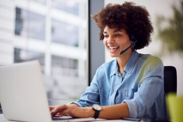 Young Businesswoman In Modern Office Working On Laptop Using Wireless Headset