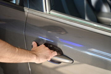 Motor vehicle owner is reaching for chrome automobile door-handle