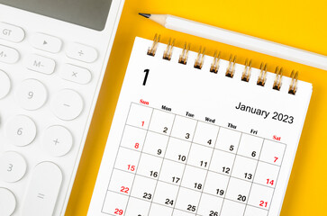 The January 2023 Monthly desk calendar for 2023 year and calculator with pen on yellow background.
