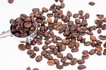 Dry coffee beans and silver spoon on white