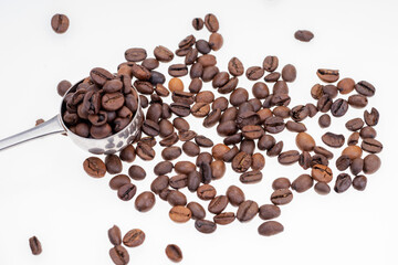 Dry coffee beans and silver spoon on white