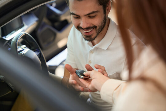 Smiling automotive buyer receiving car remote control from saleswoman