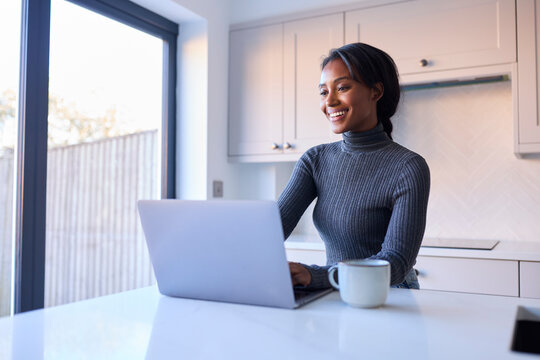 Young Woman At Home Working On Laptop On Counter In Kitchen
