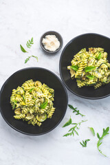 Green vegetarian fusilli pasta with zucchini pesto and herbs on a white marble background in a black bowl. Healthy and economical recipes for the whole family, Italian pasta