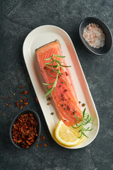 Salmon fish piece. Fresh raw salmon fish piece on marble board stand with herbs and lemon on black background. Seafood or menu concept. Top view.