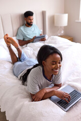 Couple At Home Streaming Film Or Movie Onto Digital Tablet And Laptop In Bed Together