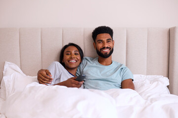 Loving Young Couple At Home Watching TV In Bed Together