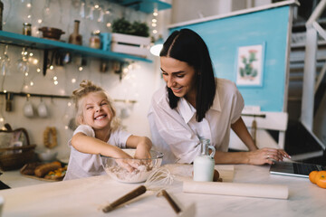 Cheerful mother and daughter preparing dough in kitchen