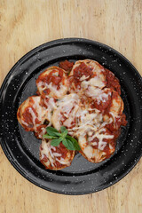 Stuffed pasta. Top view of sorrentinos with a mediterranean tomato sauce and provolone cheese in a black dish on the wooden table.