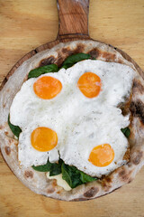 Top view of a pizza with mozzarella cheese, spinach and fried eggs, on the wooden table.	