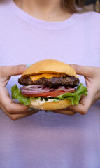 Hamburger presentation. Closeup view of a woman holding a burger with lettuce, tomato, cheddar...