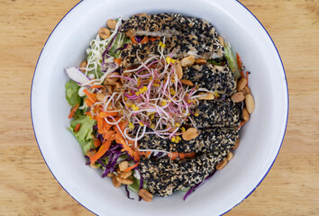 Healthy food. Top view of a salad with carrot, lettuce, peanuts, chicken breast breaded with seeds, soy sprouts and cabbage, in a white bowl on the wooden table. 