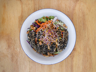 Healthy food. Top view of a salad with carrot, lettuce, peanuts, chicken breast breaded with seeds, soy sprouts and cabbage, in a white bowl on the wooden table.